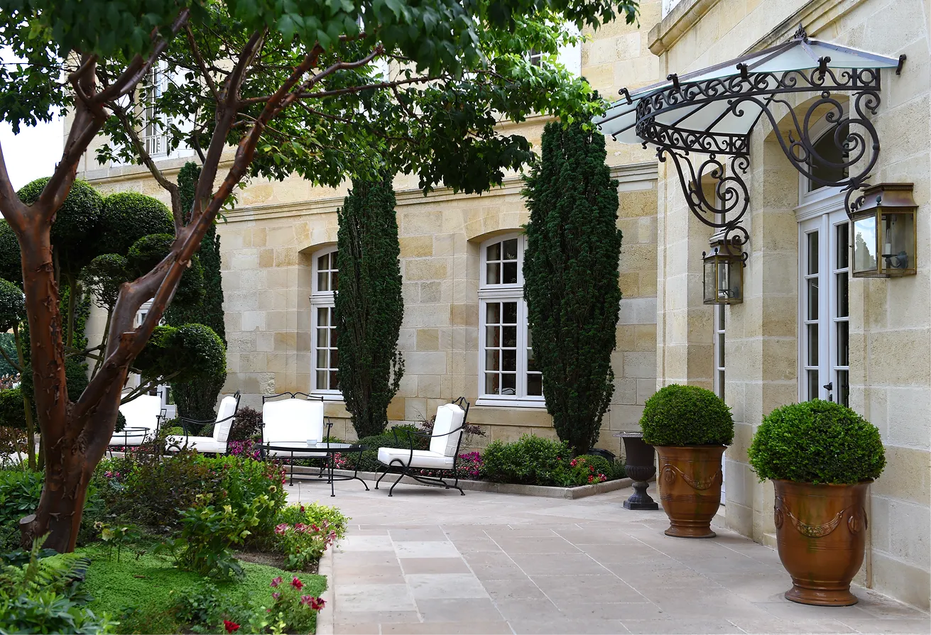 Magnifique cour d'un hôtel particulier avec des pierres de taille, des tables et des fauteuils, entourés de fleurs et d'arbres